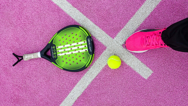 plan serr&eacute; d'une balle de padel, d'une raquette de padel d'une  basket rose sur un fond synth&eacute;tique rose