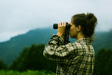 Fototapeta na wymiar A young adult female looks through binoculars in the foggy mountains