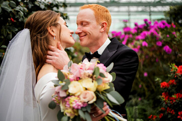 gorgeous wedding couple embracing and kissing each other in the greenhouse.