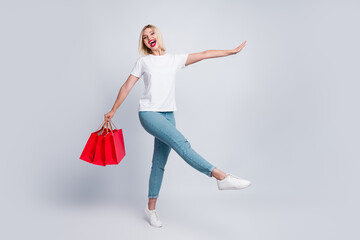 Full length photo of funky gorgeous positive girl wear stylish t-shirt jeans go shopping with red bags isolated on gray color background