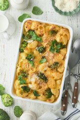 Casserole Mac and cheese. Baked Mac and cheese with broccoli, cream sauce and parmesan on white old rustic wooden background. Healthy or baby food. American Casserole Top view. Copy space.