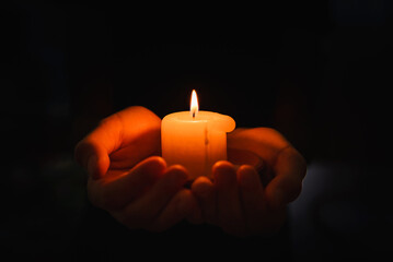 Religious concept.Boy holds in a hand a burning candle against black background.