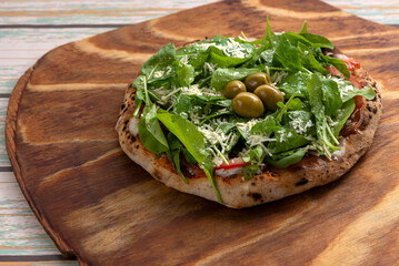 Individual homemade Neapolitan type pizzas in a clay oven with mozzarella tomato arugula ham green olives on a wooden board