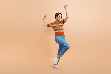 Fototapeta na wymiar Full body photo of cute cheerful young lady raise hands enjoy dancing clubbing isolated on beige color background