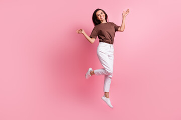 Full length photo of young active woman wearing brown t shirt and white pants raised arms up when jumping isolated on pink color background - obrazy, fototapety, plakaty