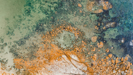 Aerial view from a drone of a natural rock pool in the sea on an Australian beach called Little Bay Beach. green and blue water color along with brown and gray colors of the reefs