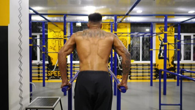 Strong african man doing push ups on parallel bars at sport club. Muscular afro american sportsman with tattoos doing hard exercises modern gym. Concept of healthy and active lifestyle. Slow motion