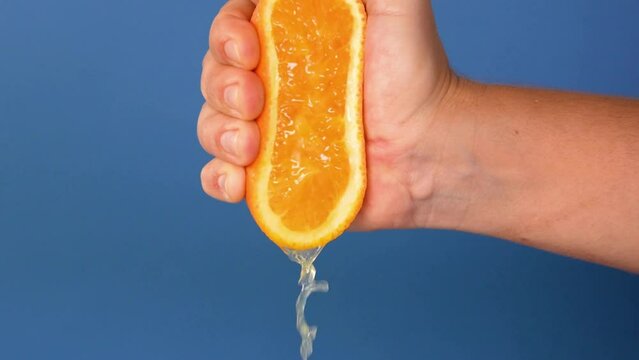 Close-up of squeezing orange juice with splashes by hand, making citrus fruit drink.