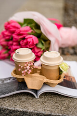 Two cups of coffee on an open magazine and pink flowers