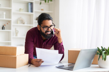 Smiling Indian freelancer verifying shipping documents while on phone call