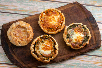 Individual tarts made of homemade dough and filled with chicken, pumpkin, carrot, mozzarella, ham and cheese on a wooden board.