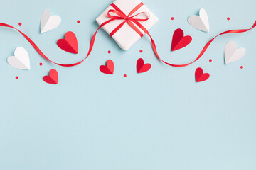 Valentine or mother day festive composition with gift or present box and red hearts on pastel blue background top view. Flat lay style. - obrazy, fototapety, plakaty