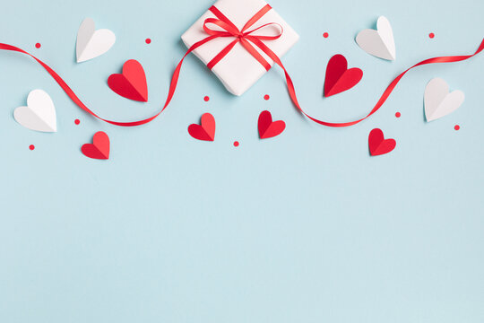 Valentine or mother day festive composition with gift or present box and red hearts on pastel blue background top view. Flat lay style.