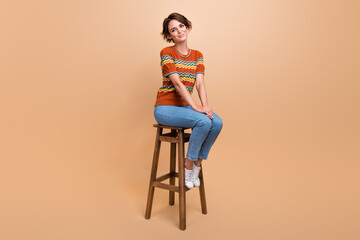 Fototapeta premium Full size photo of lovely satisfied peaceful girl sitting chair good mood isolated on beige color background