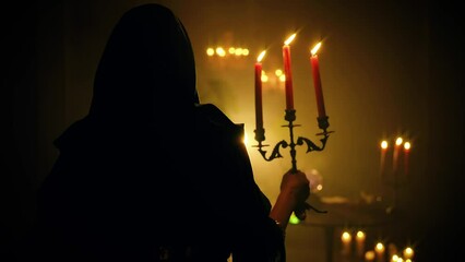 fantasy woman vampire in dark room holding old candlestick in hands candles burning warm light. Vintage style green cape dress with hood on head. Sexy girl back rear view. night black castle art. 4k