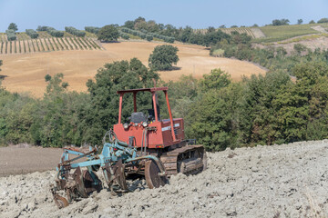old tractor with plough on ploughed filed  in green hilly countryside, near Scansano, Italy