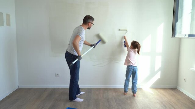 Back view father and little daughter paint wall with rollers at home. Family make renovations in new apartment. Repair