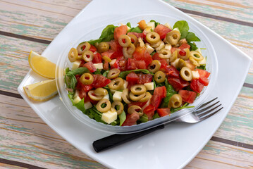 Vegetable salads with lettuce rice ham croutons tomato olives hard-boiled egg arugula carrot lemon cheese on a delivery tray on a white plate