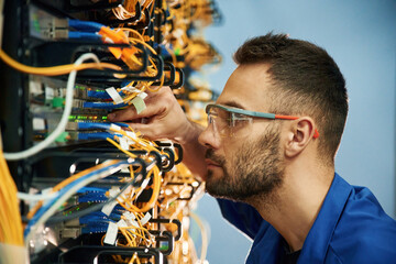 Looking extremely close at cables. Young man is working with internet equipment and wires in server...