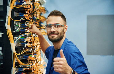 Fixed, with thumbs up. Young man is working with internet equipment and wires in server room