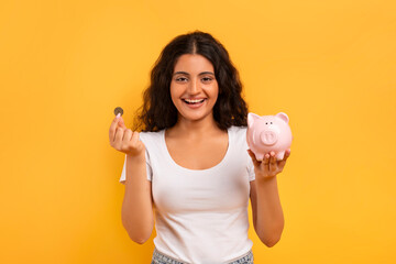 Emotional young woman with piggybank and coin on yellow