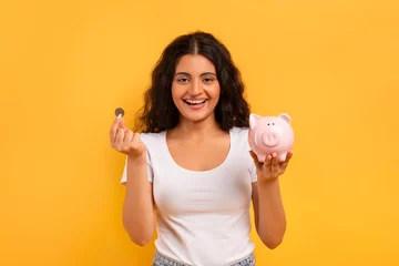 Fotobehang Emotional young woman with piggybank and coin on yellow © Prostock-studio