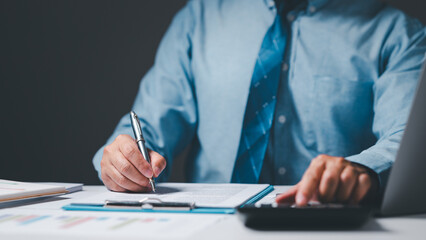 The professional businessman sits at his office desk, diligently signing business documents with a pen, illustrating the meticulous process of paperwork and decision-making in the corporate world.