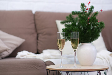 Two glasses of Champagne on caffee table in living room. Christmas home interior. Ceramic vase with fir branches.