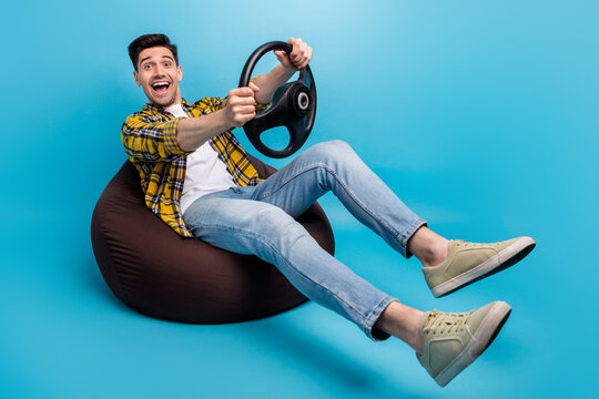 Full size body photo of young amazed guy first time sitting alone in car simulation hold steering wheel isolated on blue color background