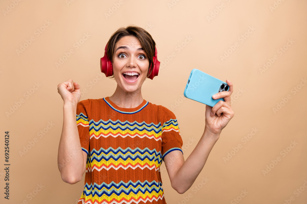 Sticker Photo of positive glad attractive girl raise fist success playing video games smart phone isolated on beige color background