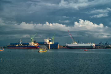 Fishings boat floats in the middle of the sea with a port and a large cargo ship in the background.