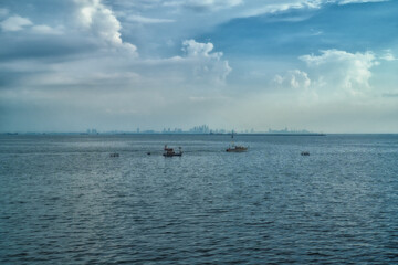 Fishings boat floats in the middle of the sea with a port and a large cargo ship in the background.