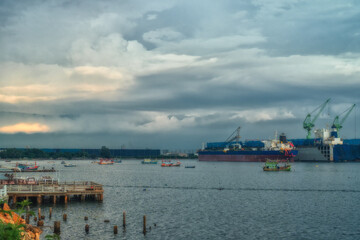 Fishings boat floats in the middle of the sea with a port and a large cargo ship in the background.