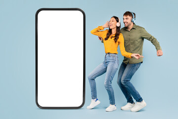 Couple with headphones dancing next to giant smartphone on blue