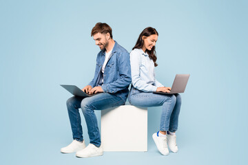 Focused couple on cube using laptops in denim attire