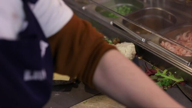 Stockholm, Sweden A male server in a cafe makes a sandwich on the stainless kitchen counter.