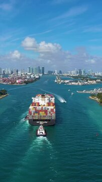 Large Container Ship Entering Port of Miami, USA. City on Sunny Day. Aerial View. Drone Flies Forward. Vertical Video