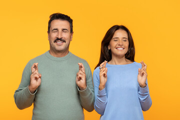 Inspired happy man and woman close their eyes and cross their fingers for luck