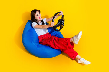 Full length photo of cheerful dreamy lady wear white t-shirt sitting bean bag driving auto empty...