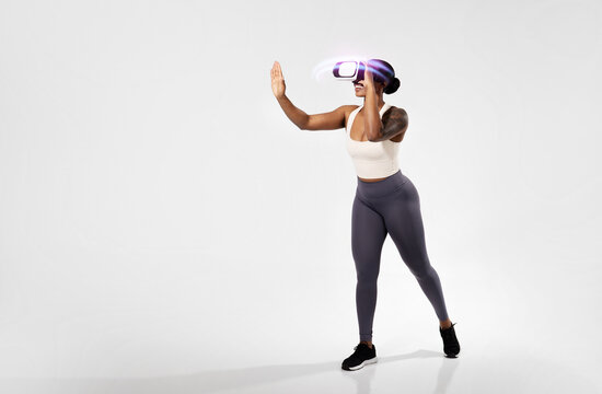 black woman working out wearing virtual reality headset, white studio