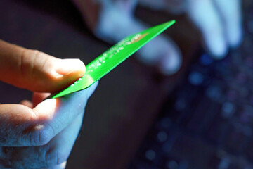 A man, holding a credit card in his hand, dials numbers to pay for online purchases using a...