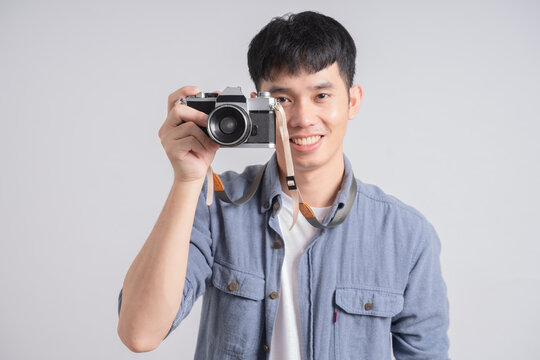 Handsome asian guy with stylish haircut taking photo on vintage camera, isolated on white background