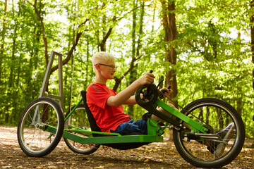 Handicapped boy riding recumbent bike at forest