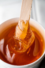 Honey-brown sugaring paste in a white plastic container with a wooden spatula