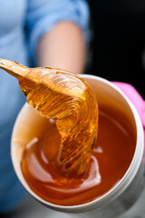 Bright honey transparent paste with a wooden spatula in a hands of specialist in a blue shirt