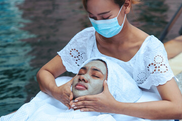 Asian female facial therapist wears face mask massaging face and applying facial mask to black...