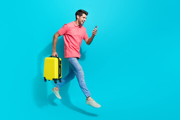 Full length photo of positive cheerful guy dressed pink polo jumping holding suitcase booking...