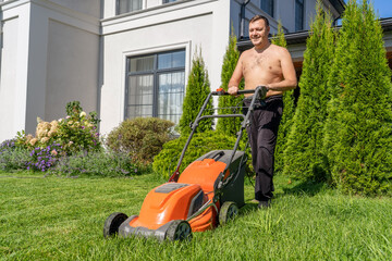 Shirtless mature man mows lawn near country house with lawn mower