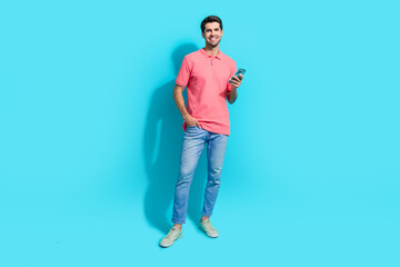 Full body photo of young handsome man wearing pink t shirt using smartphone sending proposition isolated on aquamarine color background
