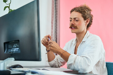 Cheerful young businessman with makeup sitting in office and working at modern computer